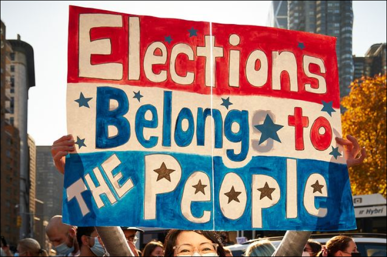 A protestor holding a sign that says "Elections Belong to the People"  Caleb Adams